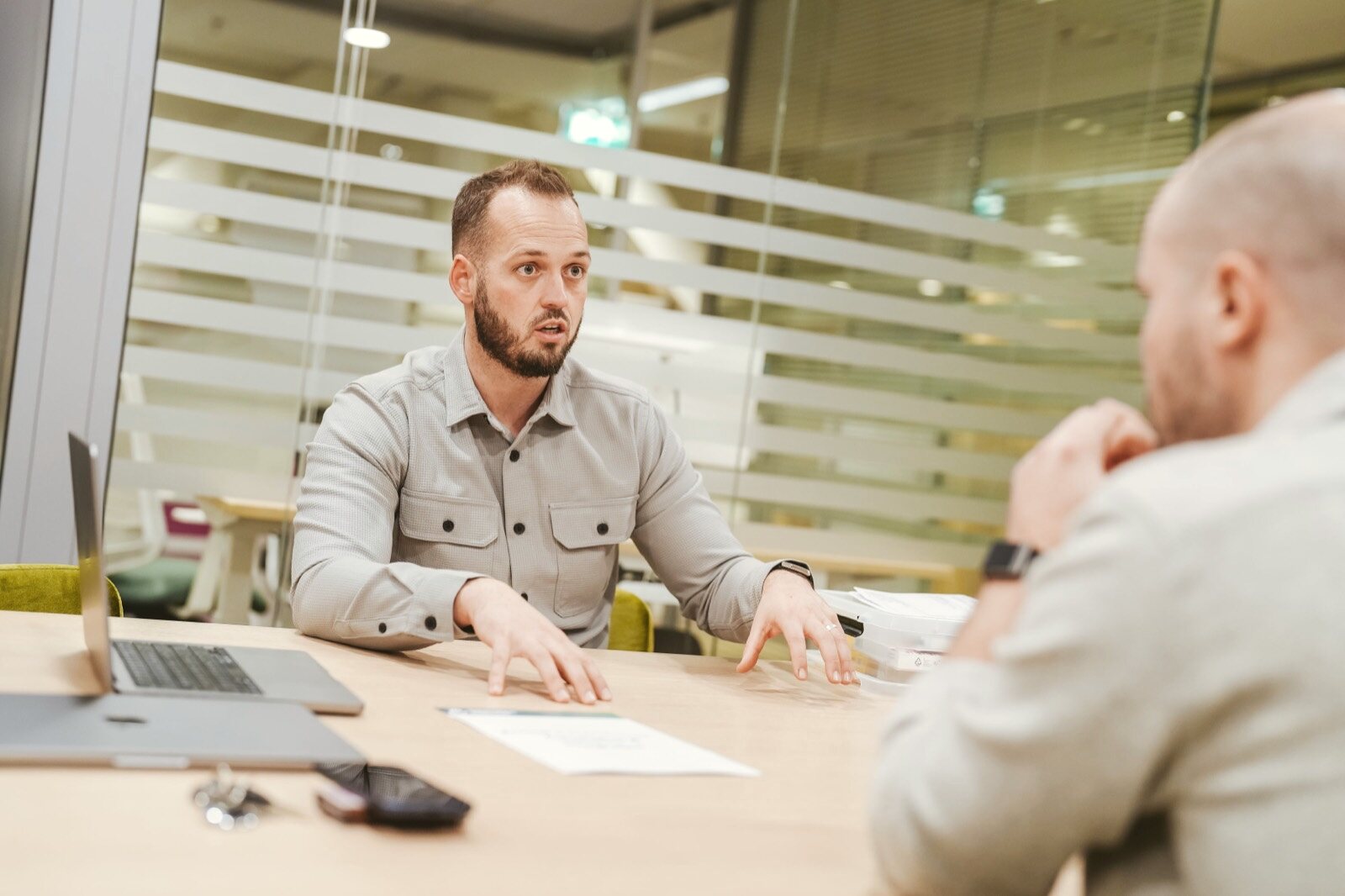 Twee mensen in gesprek aan een tafel met laptop en documenten